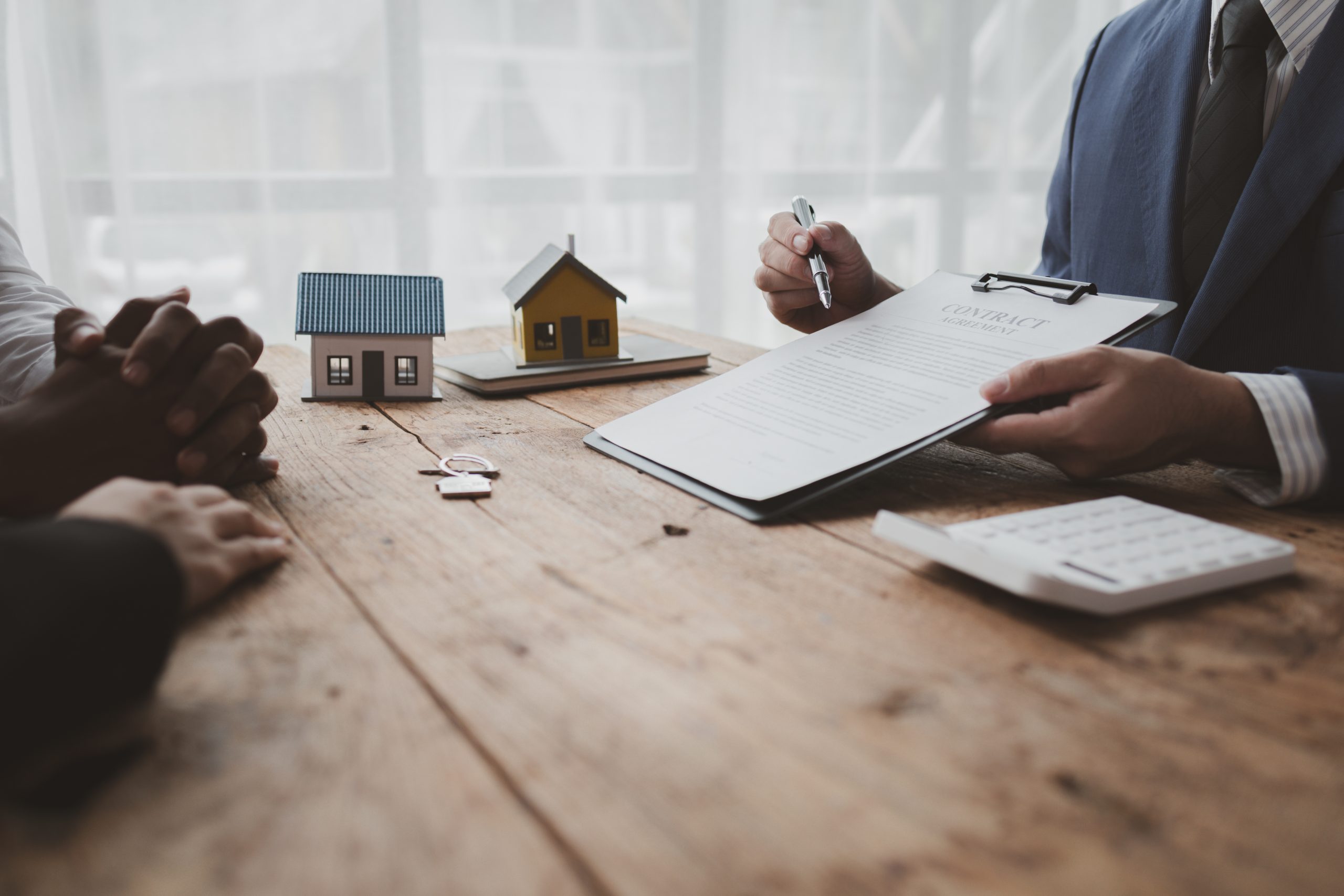 Small model houses on a wooden desk beside a laptop and documents